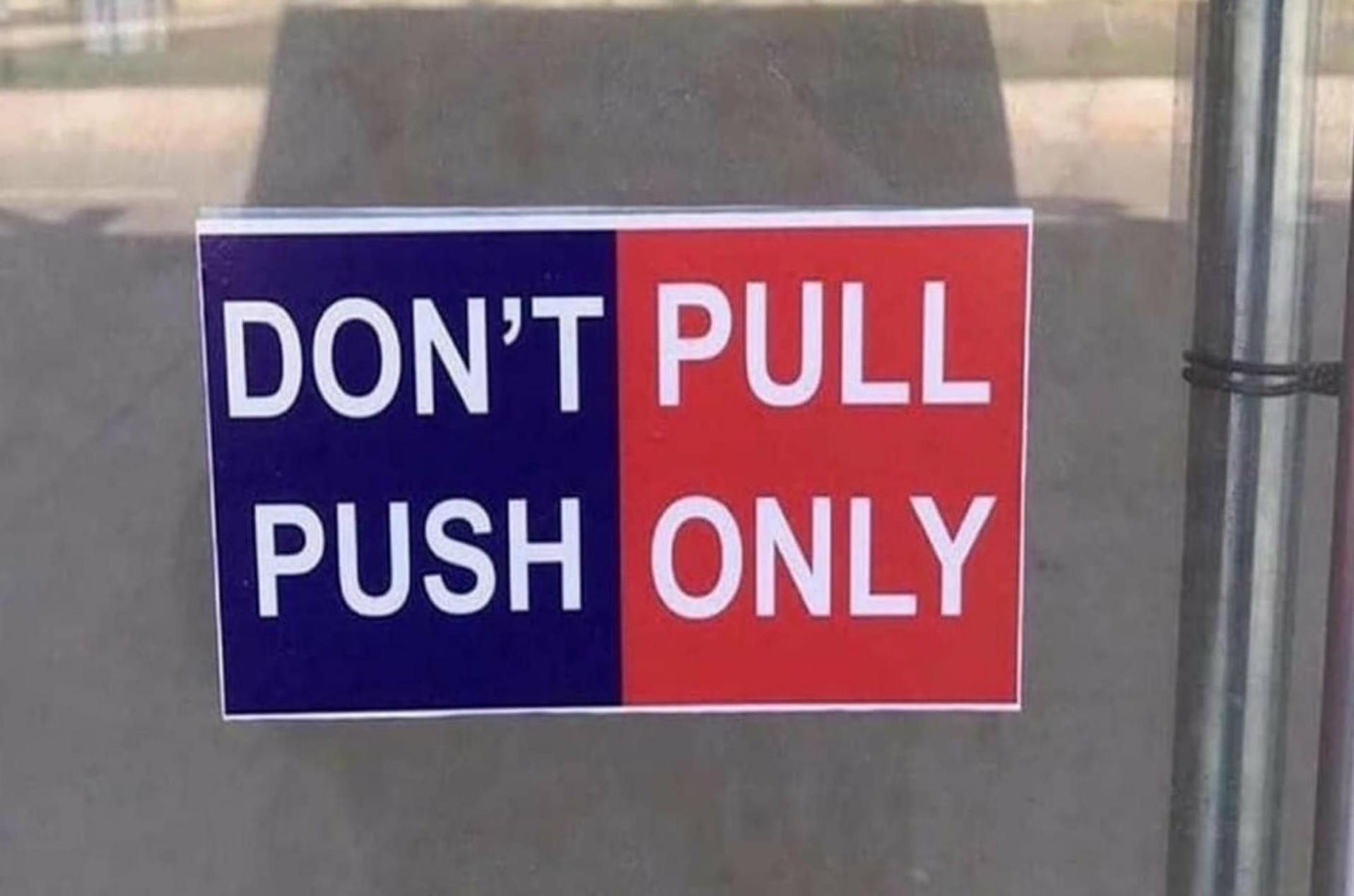 A sign hanging on a glass door that is divided vertically -- the left-hand side is colored blue and reads 'Don't Push' with the words stacked on top of one another. The right-hand side is colored red and reads 'Pull Only' with the words stacked on top of one another. However, when the sign is read left to right, top to bottom, it appears to say 'Don't Pull Push Only'.